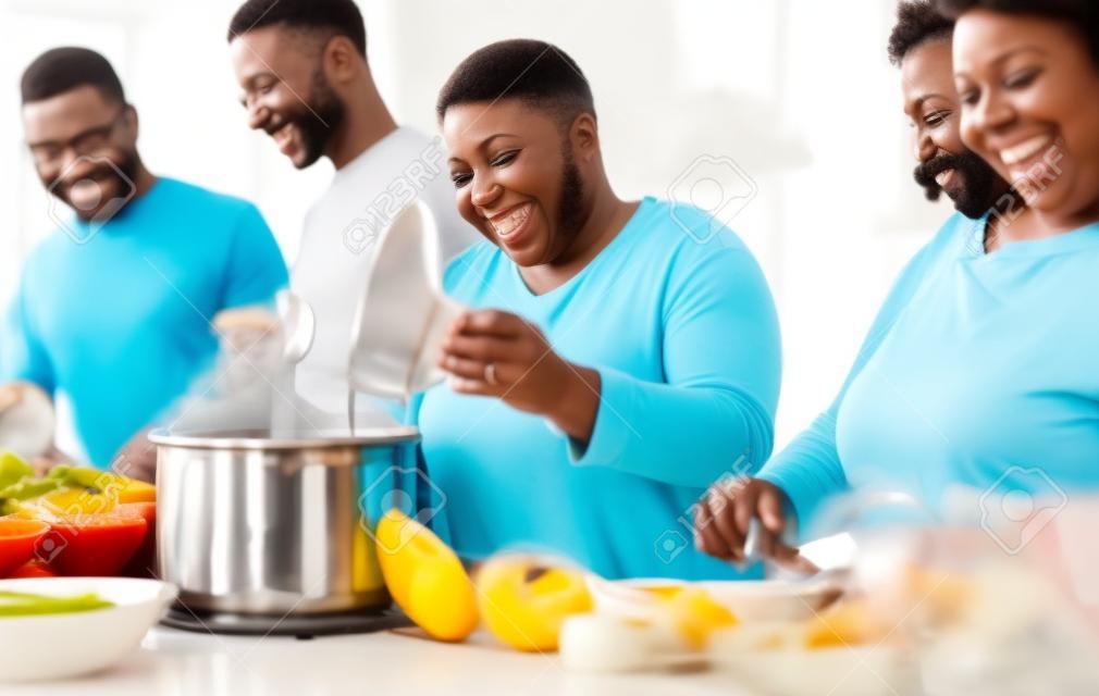 Szczęśliwa czarna rodzina bawiąca się razem gotując w nowoczesnej kuchni - koncepcja jedności jedzenia i rodziców