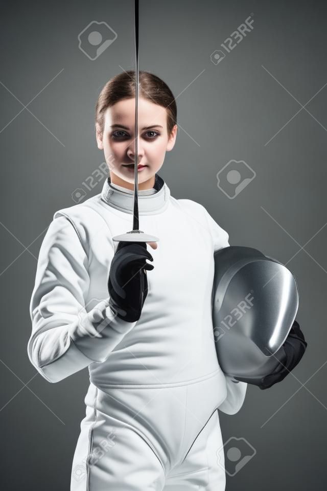 Retrato de joven mujer esgrimista vistiendo traje de esgrima blanco y sosteniendo la espada y la máscara. Mirando a la cámara. Fondo negro