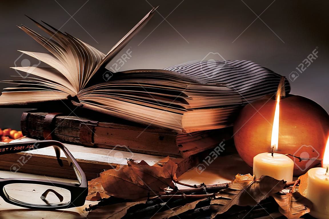책, 안경, 과일, 불타는 초, 가을 잎이 나무 테이블에 있습니다. 가 정물화입니다.