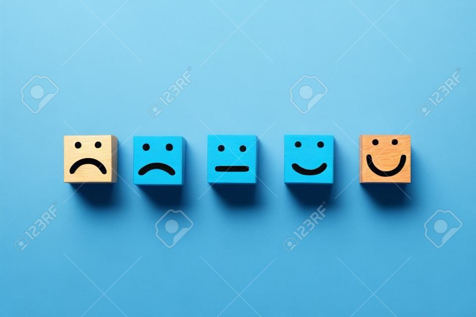 Rostro humano de pantalla de impresión triste a sonrisa en la cara de un cubo de bloque de madera sobre fondo azul para un pensamiento positivo y una excelente calificación de evaluación después del uso del concepto de producto y servicio