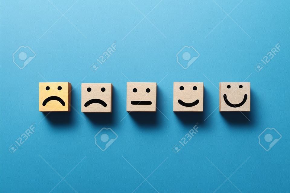 Rostro humano de pantalla de impresión triste a sonrisa en la cara de un cubo de bloque de madera sobre fondo azul para un pensamiento positivo y una excelente calificación de evaluación después del uso del concepto de producto y servicio