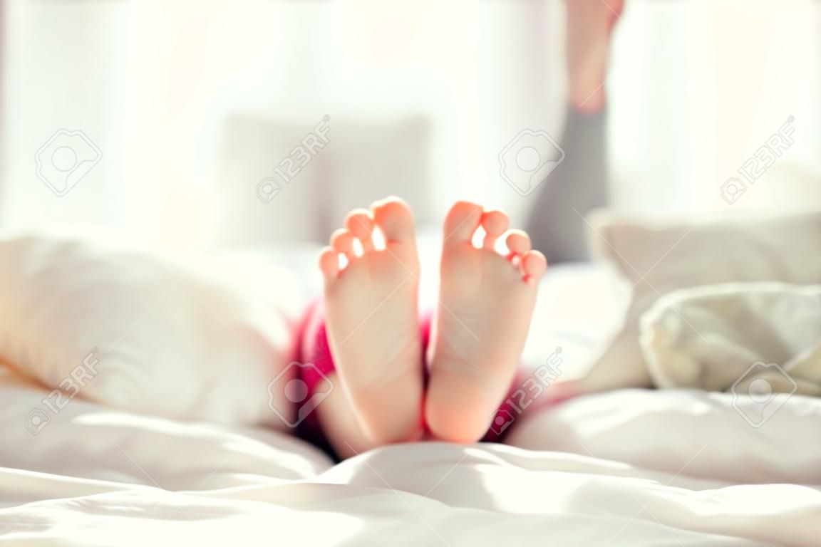 Piedi bambino su manto bianco sul letto. Adorabile bambina si sveglia nel suo letto. mattina. Ritratto dei piedi dei bambini in camera da letto