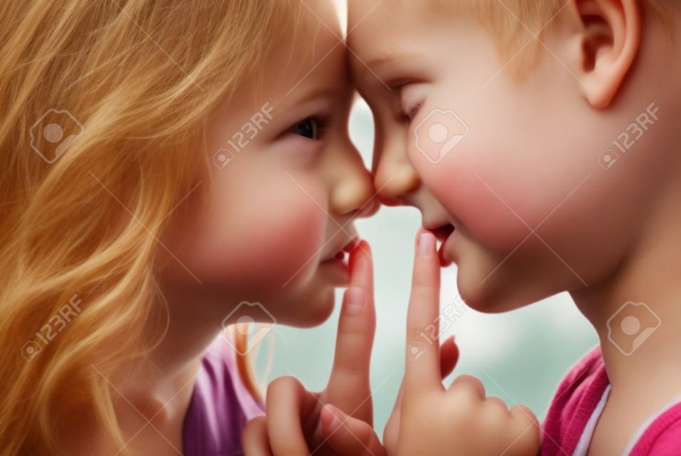Garçon et fille debout face à face avec les doigts sur leurs lèvres.