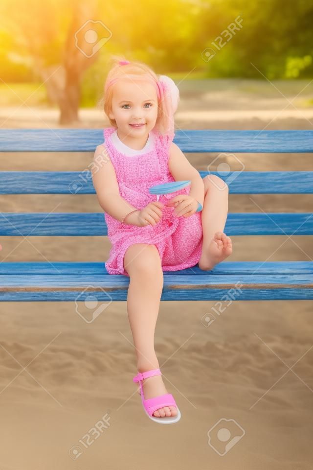 坐在一张旧长凳上的漂亮女孩摇着触发器上的沙子
