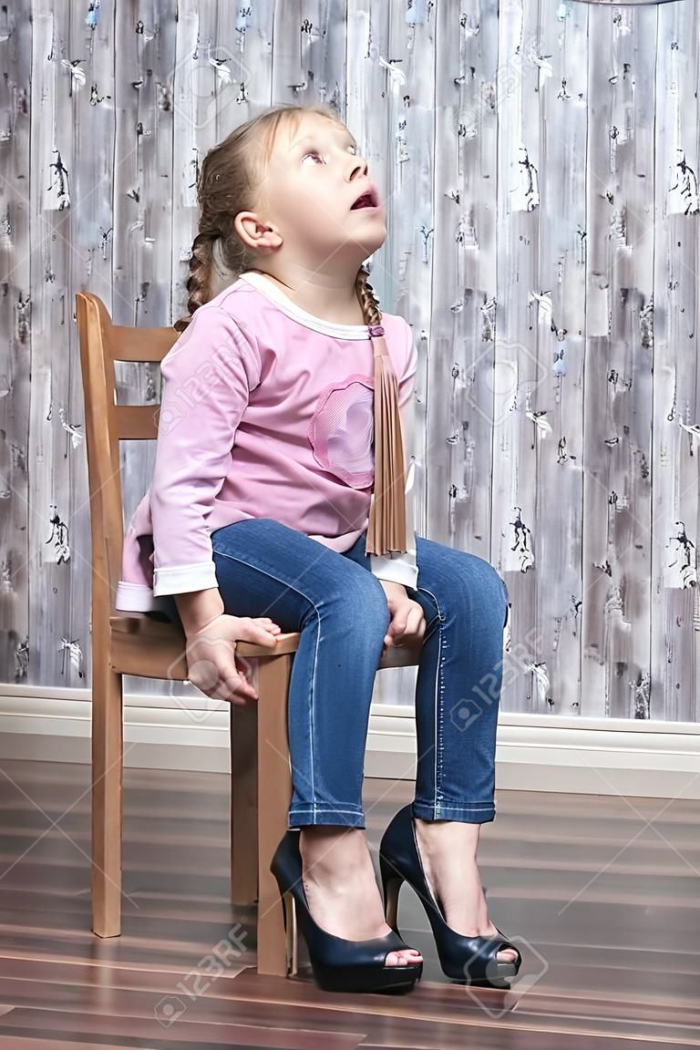 jong meisje zittend op een houten stoel ziet er gefrustreerd uit het proberen van haar moeder hoge hakken schoenen