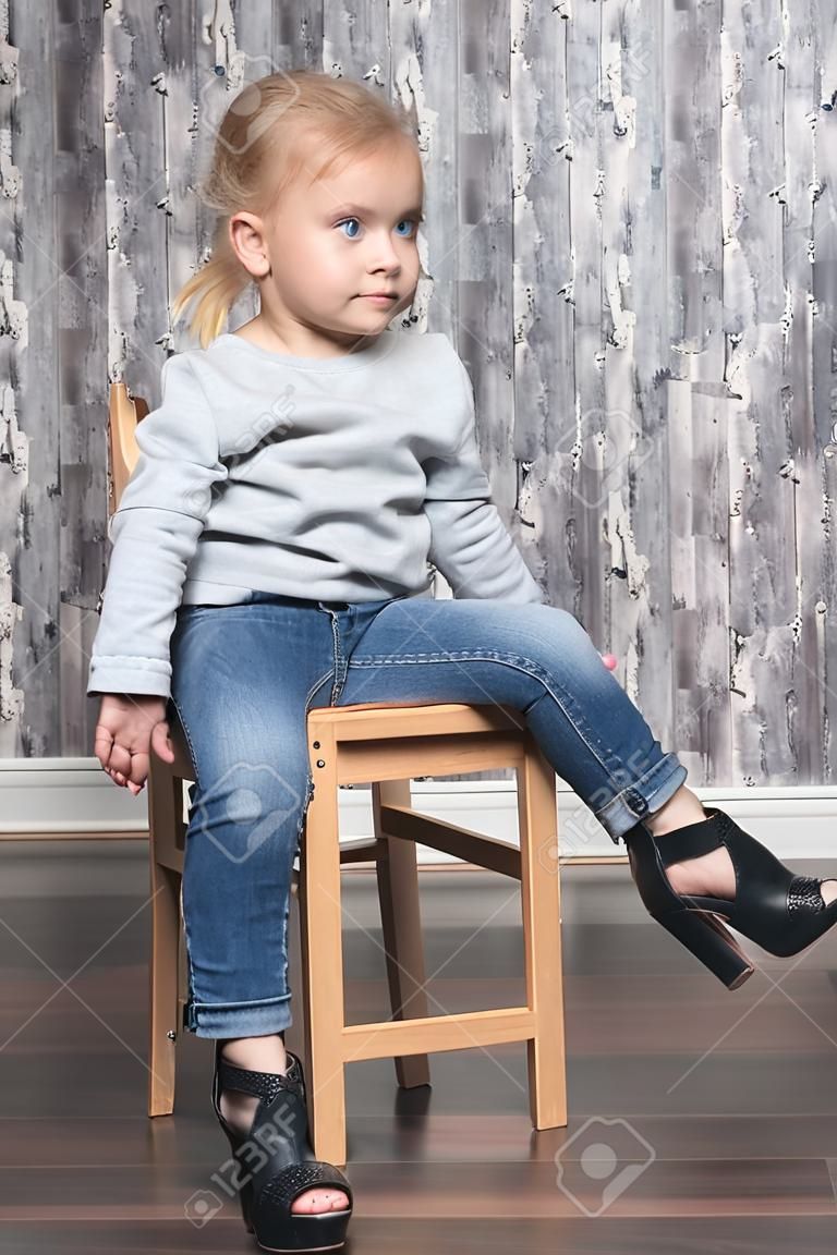 baby girl sitting on a wooden chair, legs wearing her mother big shoes