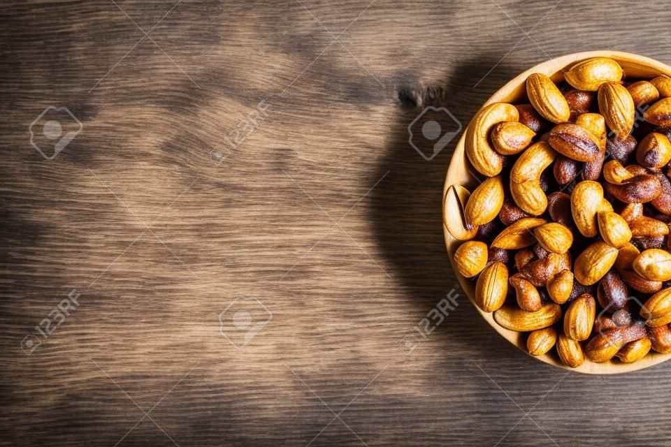 Cacahuetes tostados con cáscara y pelados en una taza marrón, contra una mesa de madera gris. Proteína vegetariana orgánica, macro.