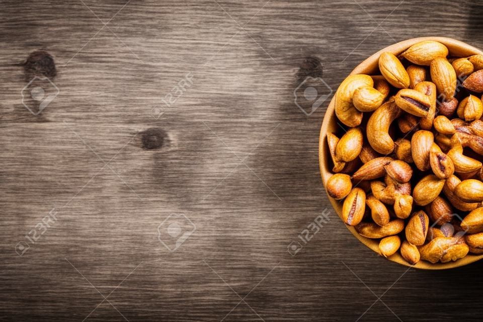 Roasted peanuts in their shells and peeled in a brown cup, against a gray wooden table. Organic vegetarian protein, macro.
