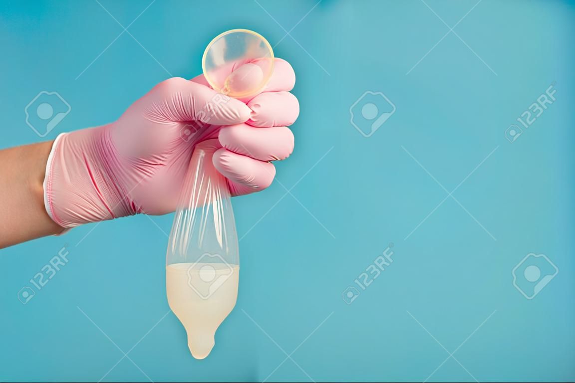 Anticoncepción de condón de látex con esperma, un médico con un guante rosa sostiene un condón usado completo sobre un fondo azul.
