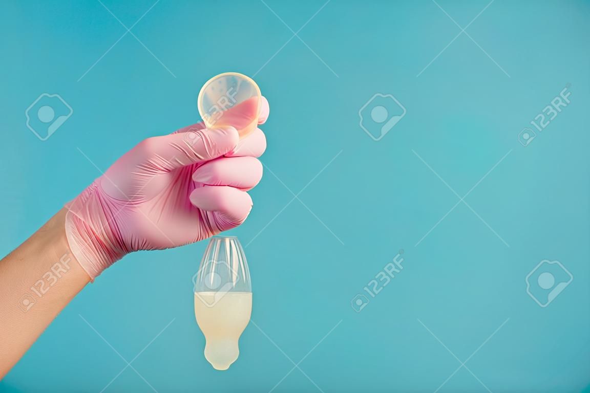 La contraccezione del preservativo in lattice con lo sperma, un medico con un guanto rosa tiene un preservativo completamente usato su uno sfondo blu