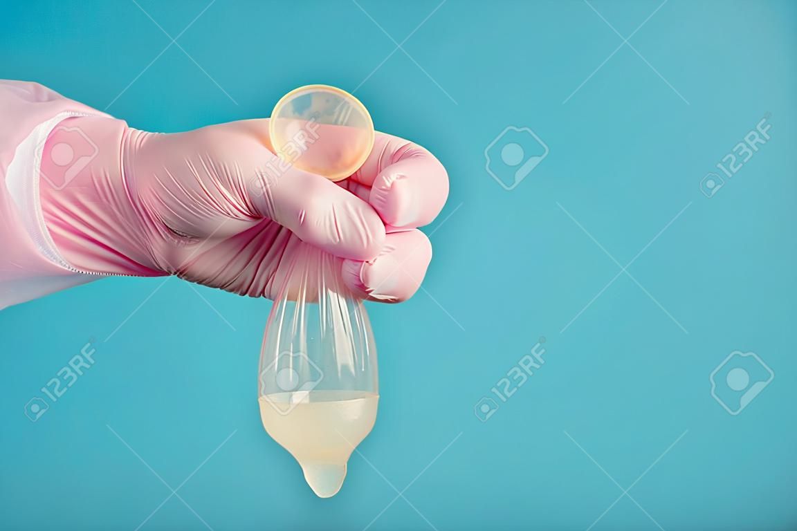 Latex condoom anticonceptie met sperma, een arts in een roze handschoen heeft een volledig gebruikt condoom op een blauwe achtergrond