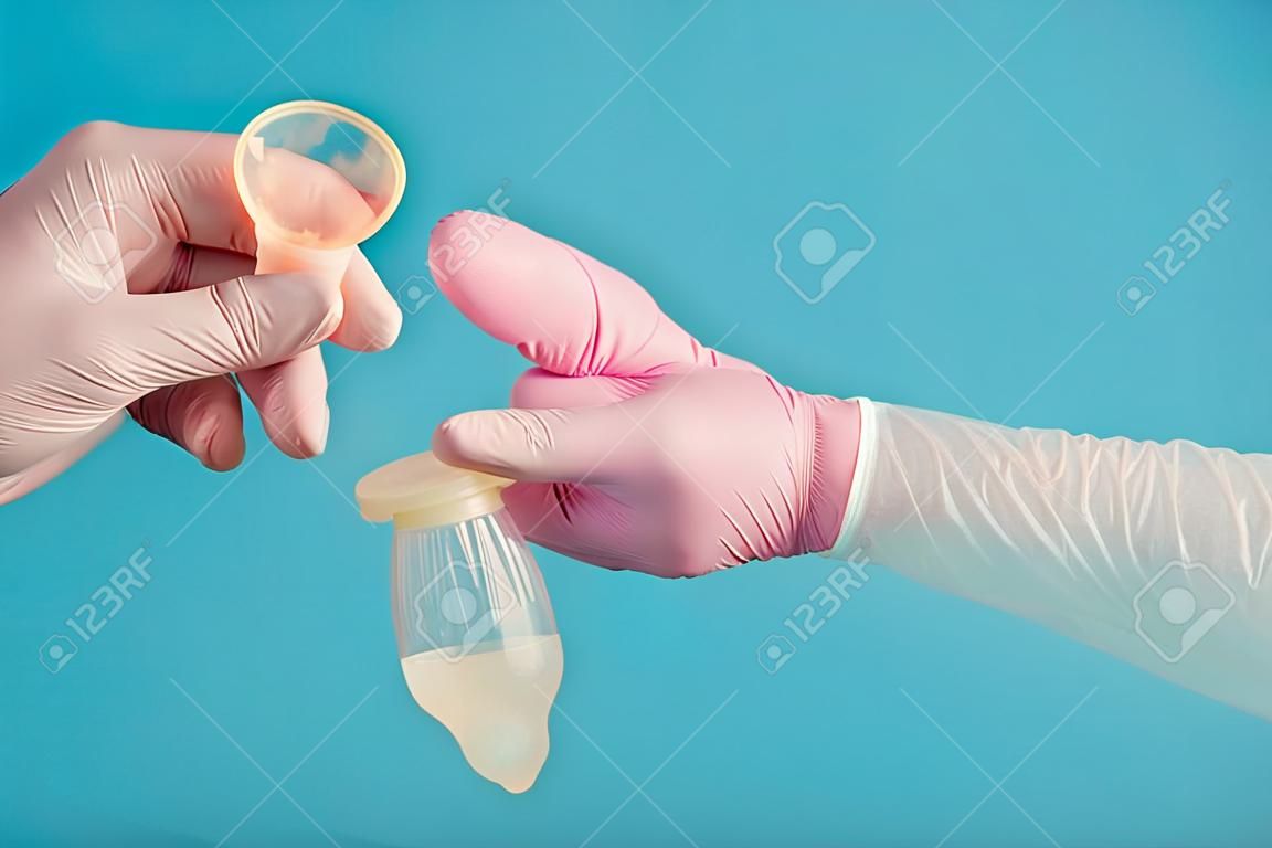 Anticoncepción de condón de látex con esperma, un médico con un guante rosa sostiene un condón usado completo sobre un fondo azul.