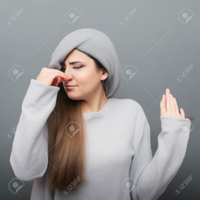 Portrait of woman covering nose with hand showing that something stinks against gray background