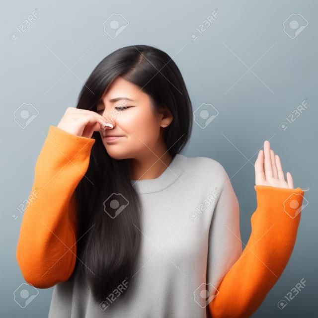 Portrait of woman covering nose with hand showing that something stinks against gray background