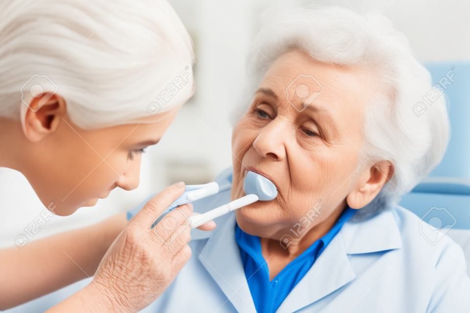 Arzt untersucht ältere Frau bei Halsschmerzen