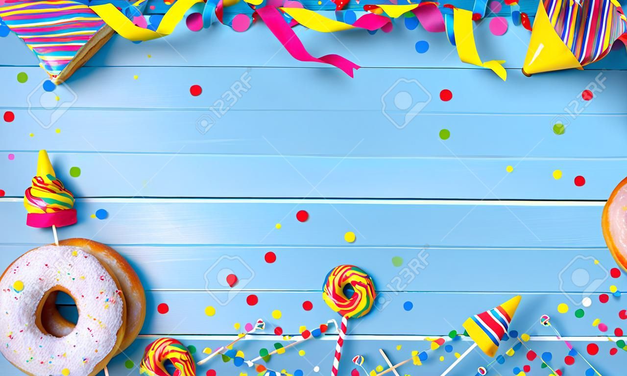 푸른 나무 판자에 깃발, 색종이 조각 및 기타 파티 액세서리가 있는 크라펜, 베를린 또는 도넛. 화려한 카니발 또는 생일 배경