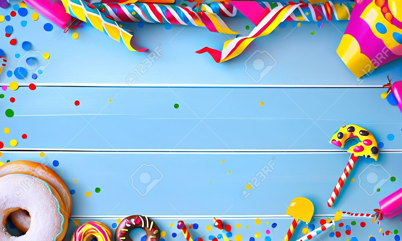 Krapfen, berliner ou beignets avec banderoles, confettis et autres accessoires de fête sur des planches en bois bleues. Carnaval coloré ou fond d'anniversaire