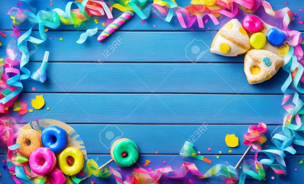 Krapfen, berliner o donuts con serpentinas, confeti y otros accesorios para fiestas en tablones de madera azul. Fondo colorido carnaval o cumpleaños