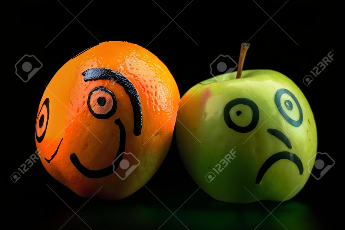 печальное яблоко с счастливым оранжевой маской на черном фоне