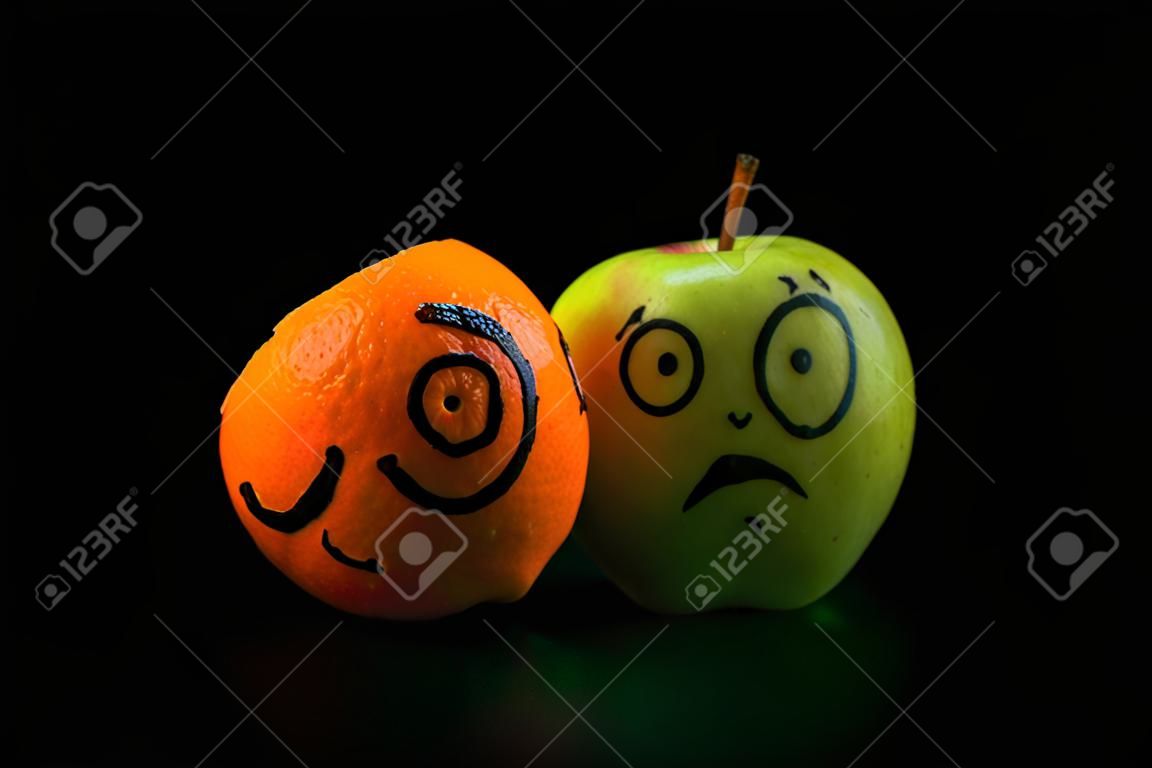 печальное яблоко с счастливым оранжевой маской на черном фоне