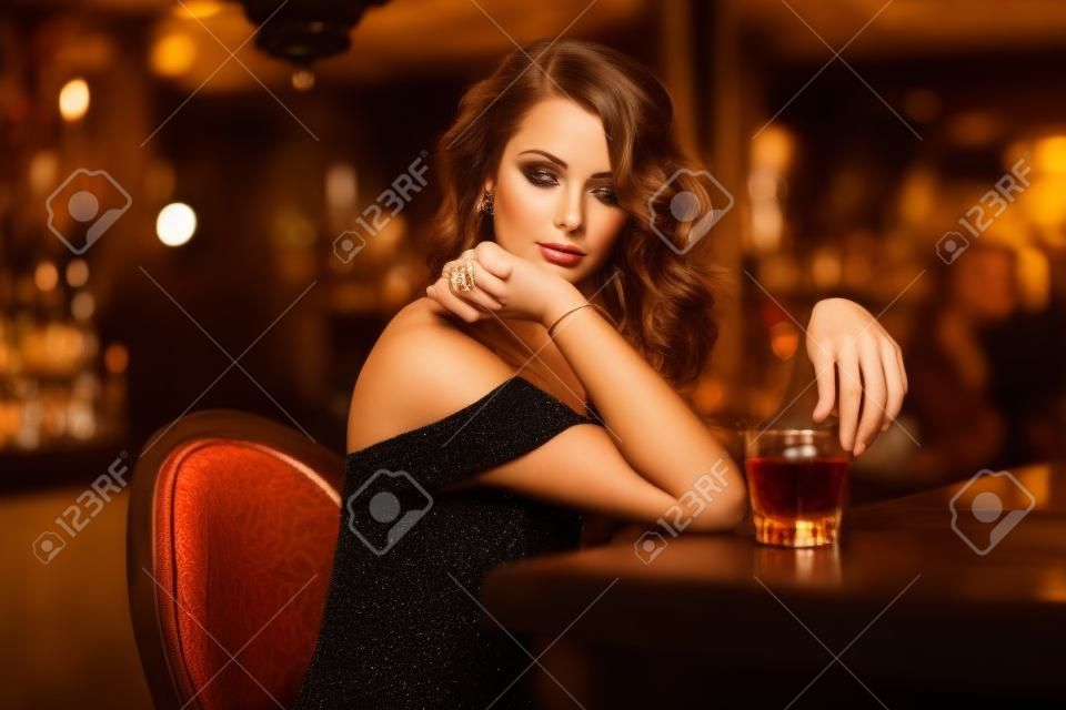 Beauty junge Frau Brünette an der Bar mit einem Glas Whiskey in Luxus-Interieur sitzt