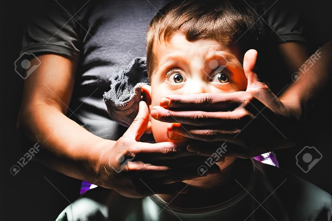 Male hands cover mouth of scared boy child trafficking victim kidnapping concept on black background
