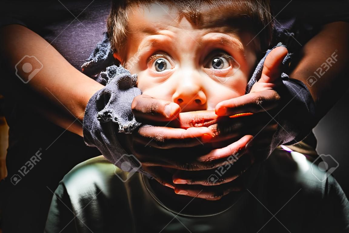 Male hands cover mouth of scared boy child trafficking victim kidnapping concept on black background