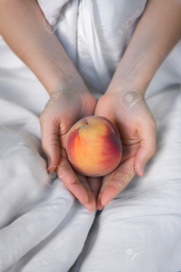 Close up hands of woman farmer holds ripe peaches on linen dress background.