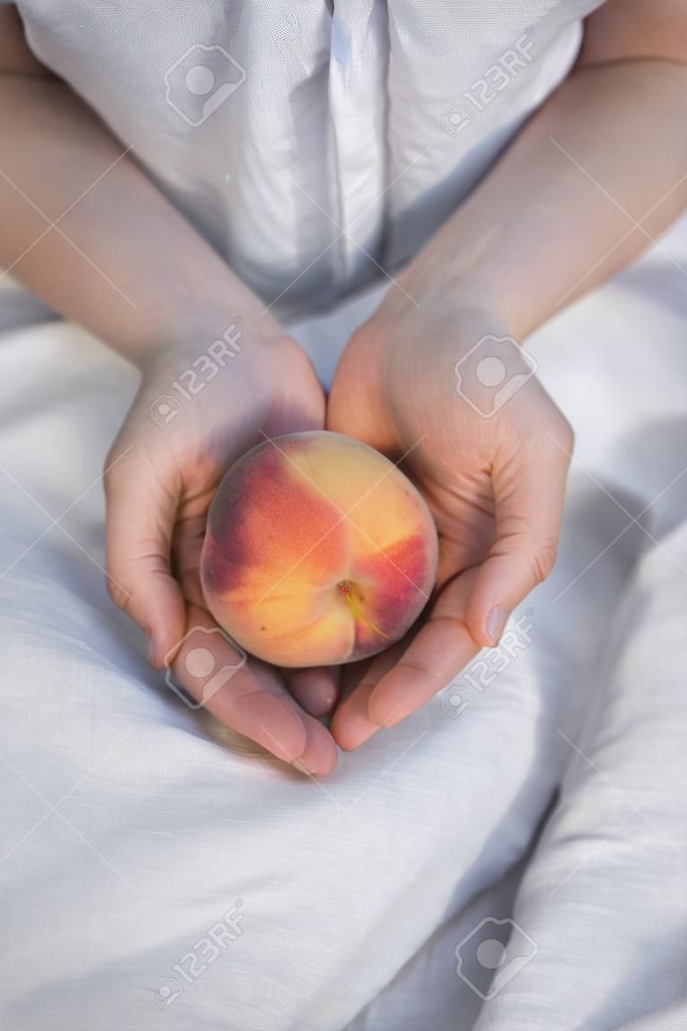 Close up hands of woman farmer holds ripe peaches on linen dress background.