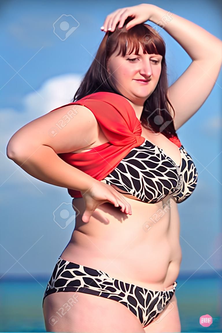 Mujer en traje de baño en el mar. Mujer joven gorda desnuda en aire libre, mirando a la cámara sonriendo