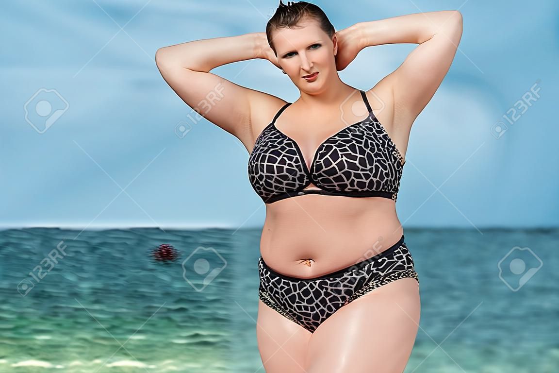 海で水着の女性。水の上の地平線に対するポーズの水着で若い女性を太りすぎ。腕を上げた女性カメラ目線彼女の髪を修正します。