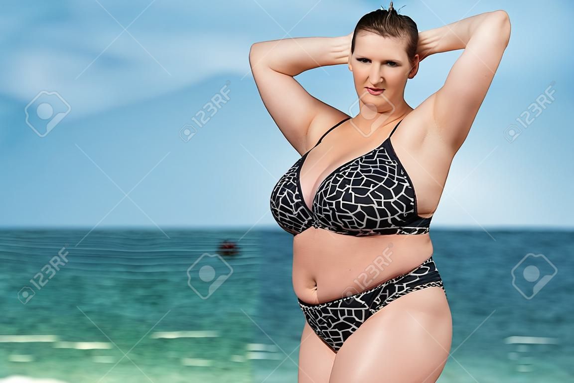 海で水着の女性。水の上の地平線に対するポーズの水着で若い女性を太りすぎ。腕を上げた女性カメラ目線彼女の髪を修正します。