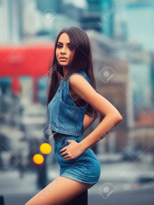 Atrakcyjna dziewczyna hipster w strojach casual siedzi na miejskim tle. Moda, koncepcja młodzieży.