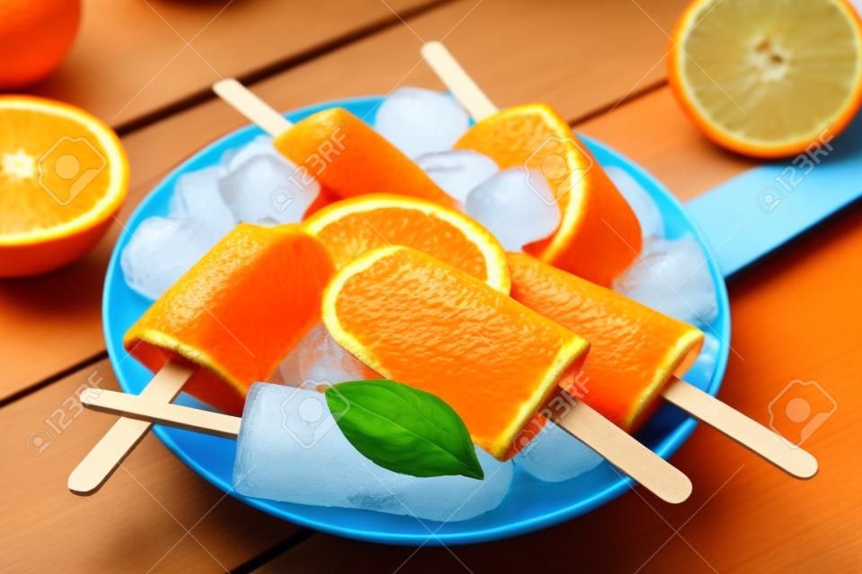 Orange  on blue wooden background. Summer refreshing ices on stick.