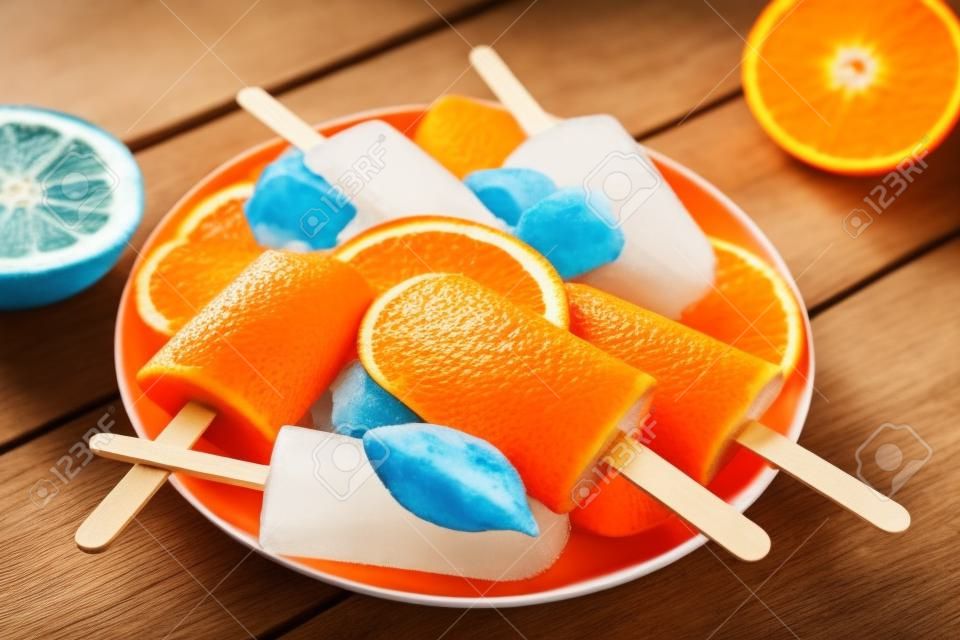 Orange  on blue wooden background. Summer refreshing ices on stick.
