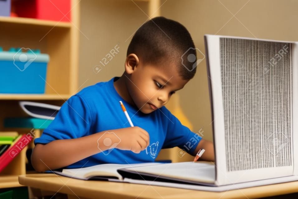 Kind macht seine Hausaufgaben mit Notebook und Lehrbuch
