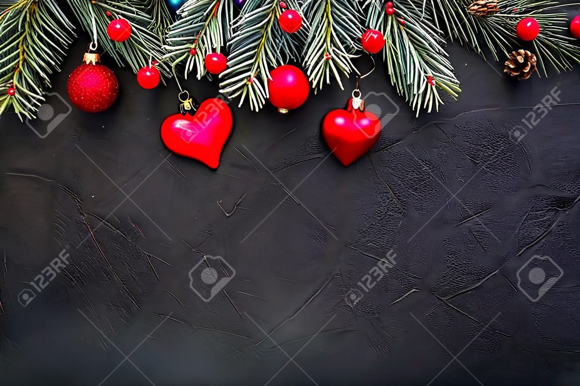 Sfondo di Natale: rami di abete verde, giocattoli rossi e un giocattolo a forma di cuore, su uno sfondo nero con texture. Modello per il design, biglietto di auguri, saluto. Vista dall'alto. Lay piatto
