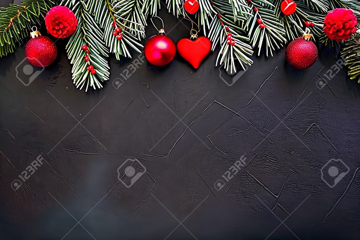 Sfondo di Natale: rami di abete verde, giocattoli rossi e un giocattolo a forma di cuore, su uno sfondo nero con texture. Modello per il design, biglietto di auguri, saluto. Vista dall'alto. Lay piatto
