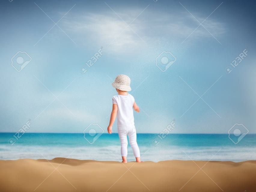 Lilltle boy looking at the ocean, playing on the seaside in summertimes. Baby having fun with the sand. Summer rest concept. Happy childhood concept