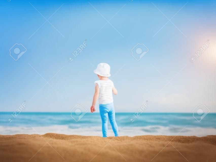 Lilltle boy looking at the ocean, playing on the seaside in summertimes. Baby having fun with the sand. Summer rest concept. Happy childhood concept
