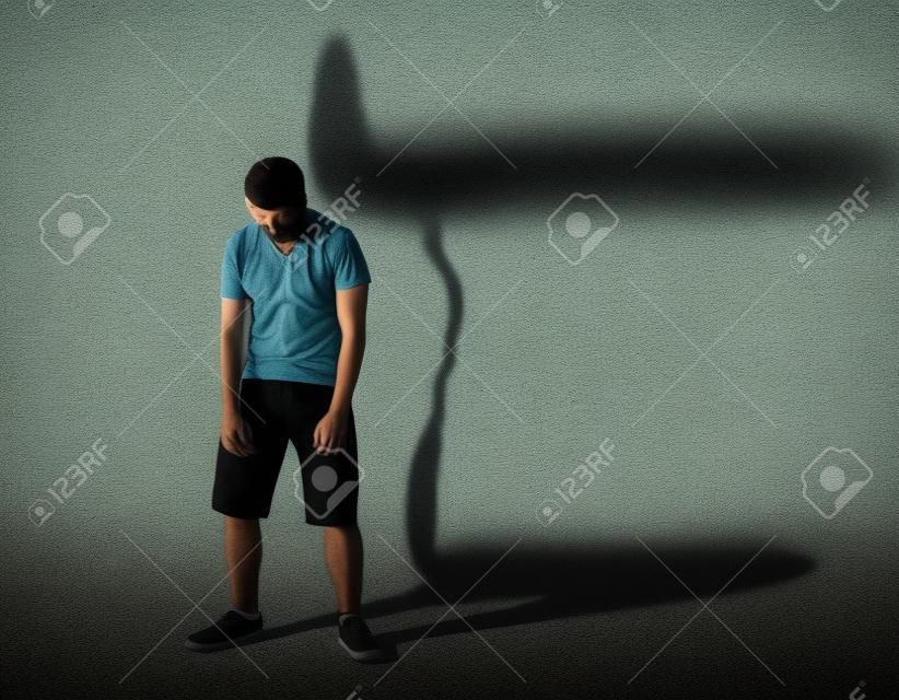 Image d'un homme faible debout déprimé en face d'un mur et son ombre montre streght