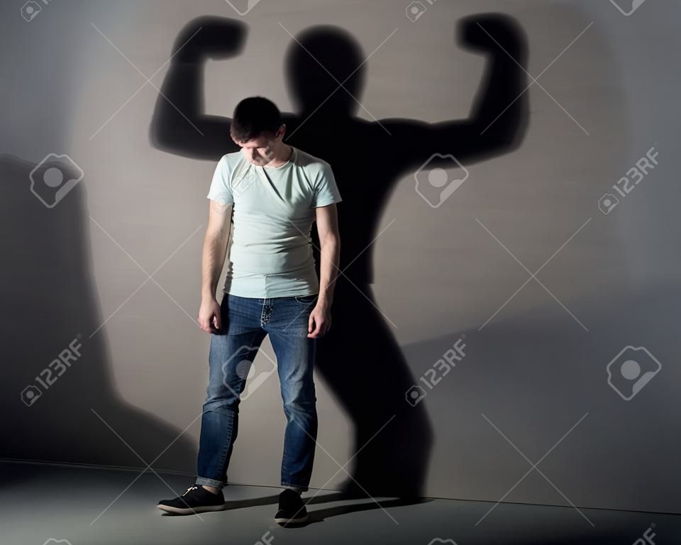 Bild eines schwachen Mann, der vor einer Wand gedrückt und sein Schatten zeigt streght