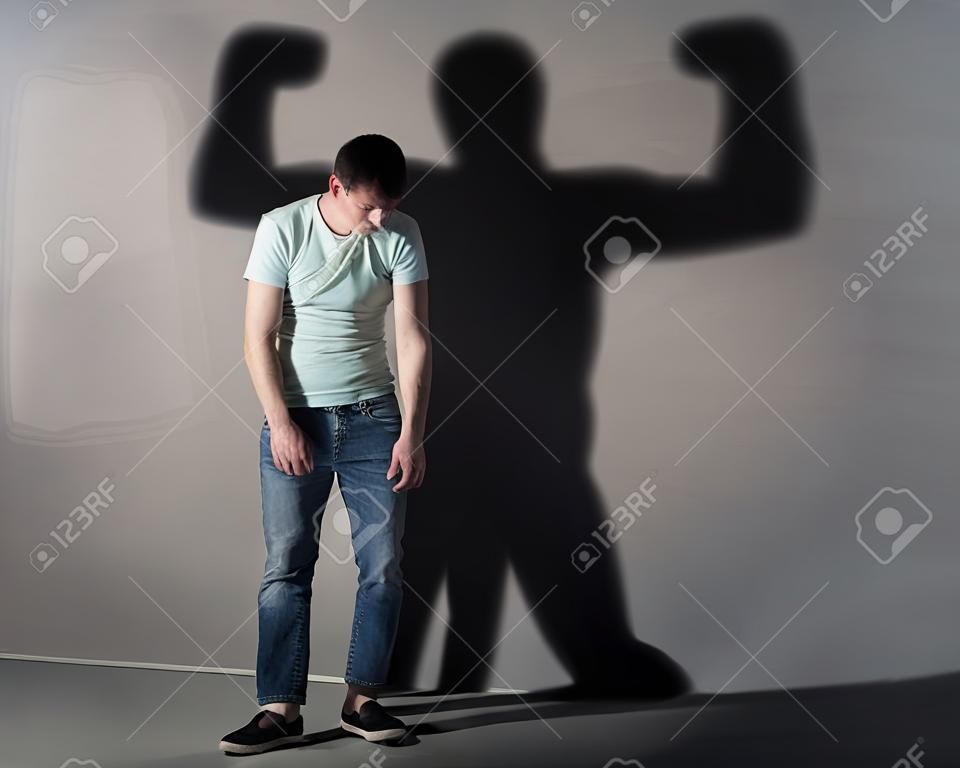 Bild eines schwachen Mann, der vor einer Wand gedrückt und sein Schatten zeigt streght