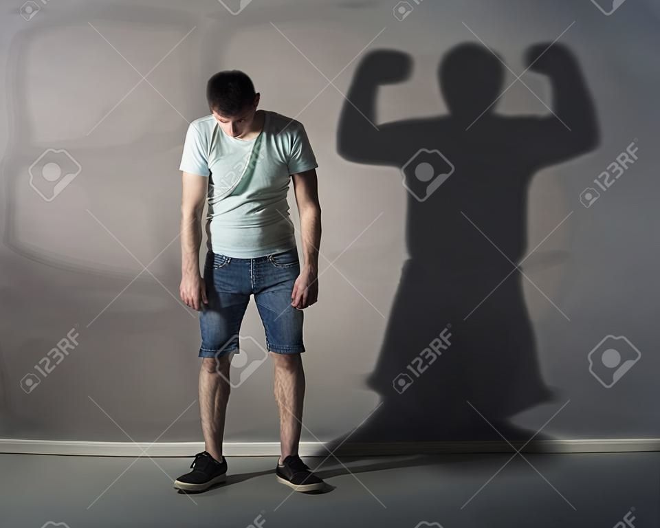 Image d'un homme faible debout déprimé en face d'un mur et son ombre montre streght