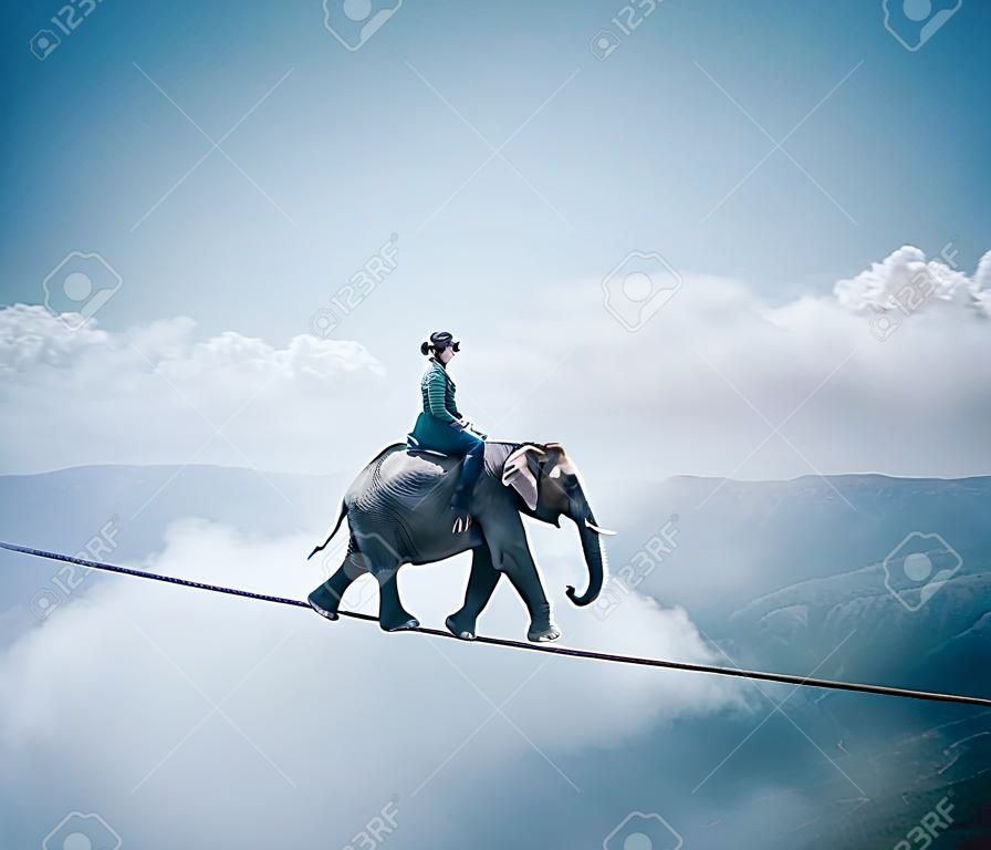 Young woman riding an elephant on a rope at high altitude, above clouds and mountains.