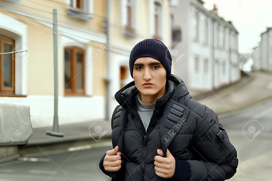 Handsome young man in winter jacket and knitted black hat on city background
