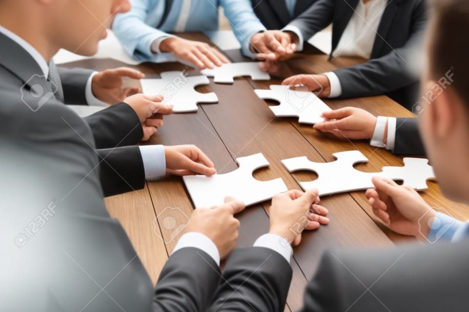 Pessoas de negócios e quebra-cabeça na mesa de madeira, conceito de trabalho em equipe