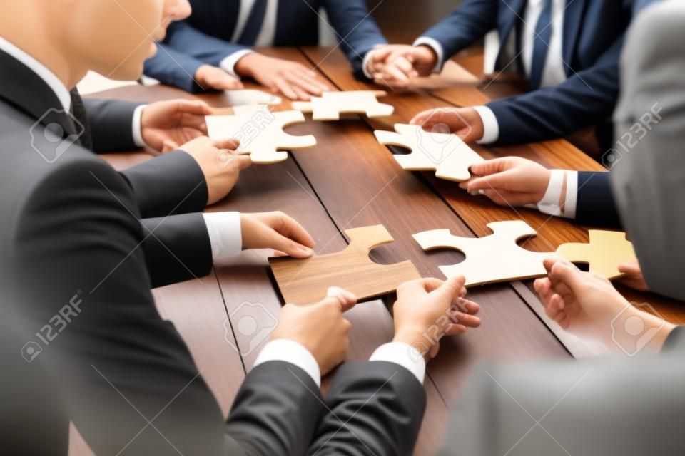Gli uomini d'affari e di puzzle sul tavolo in legno, concetto di lavoro di squadra