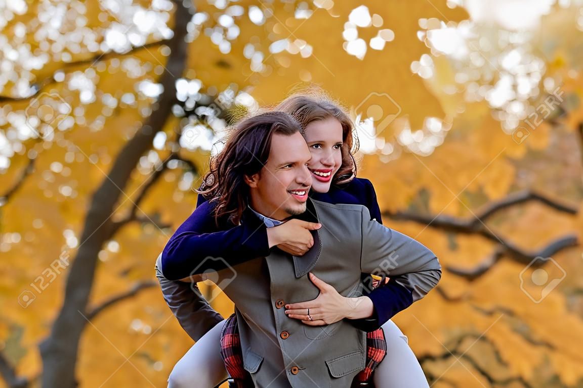 pareja, en, otoño, parque, tener diversión, sonriente, hombre, proceso de llevar, mujer, piggyback, al aire libre