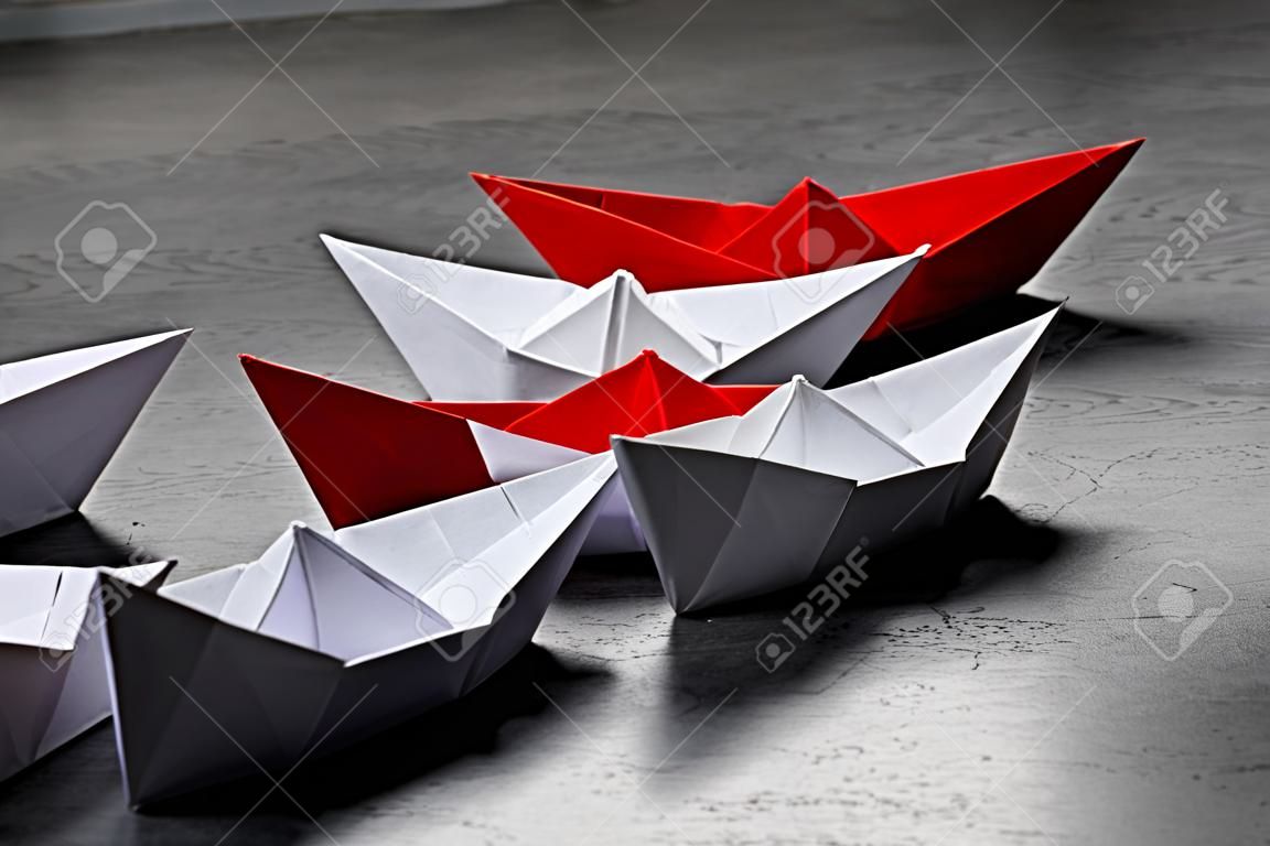 Business Concept, Paper Boat, the key opinion Leader, the concept of influence. One red paper boat as the Leader, leading in the direction of the white ships on a gray concrete background,copy space